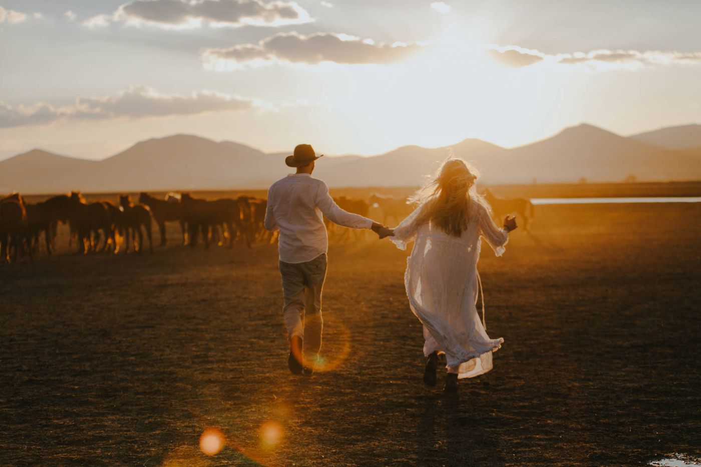 Couple running hand in hand toward a herd of wild horses at sunset near Cappadocia